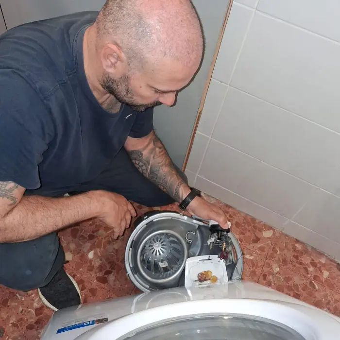 Técnico de Electro González vaciando manualmente una lavadora que no desagua debido a un tapón de monedas en L'Hospitalet de Llobregat