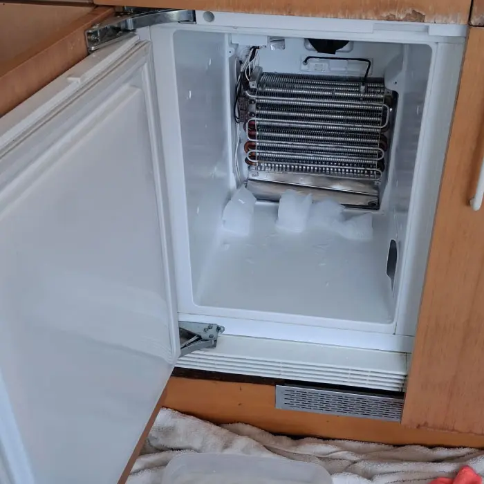 Técnico de Electro González desarmando el panel interior de una nevera obstruida por placas de hielo en Barcelona.